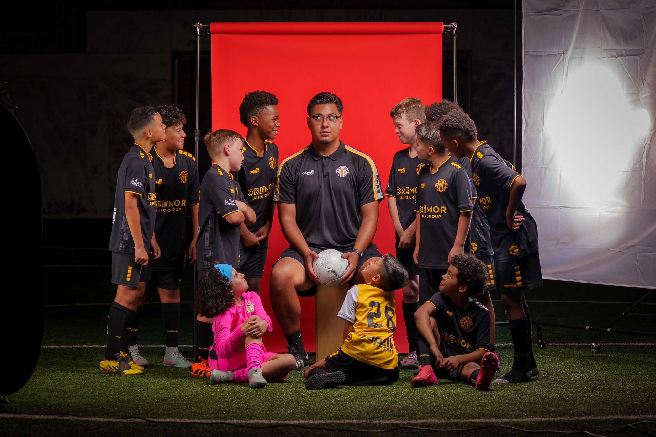 Youth soccer team photo session with red backdrop and studio lighting setup.