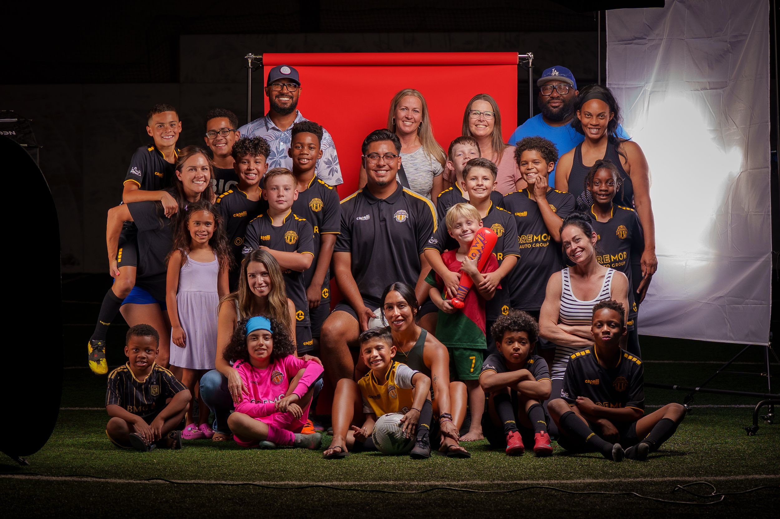 Large group photo of soccer players and parents against red and white backdrop.