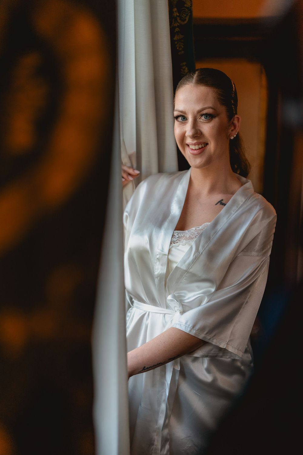 Close-up portrait of someone in a white satin robe smiling warmly against a dark background.