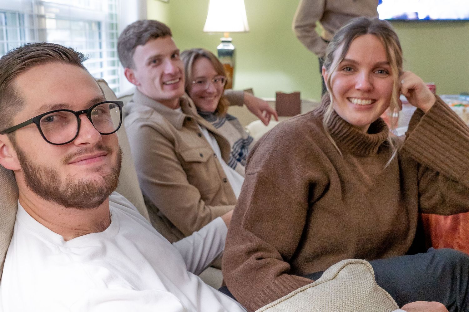 A group of friends relaxing together on a couch in a living room, wearing cozy sweaters and sharing laughs.