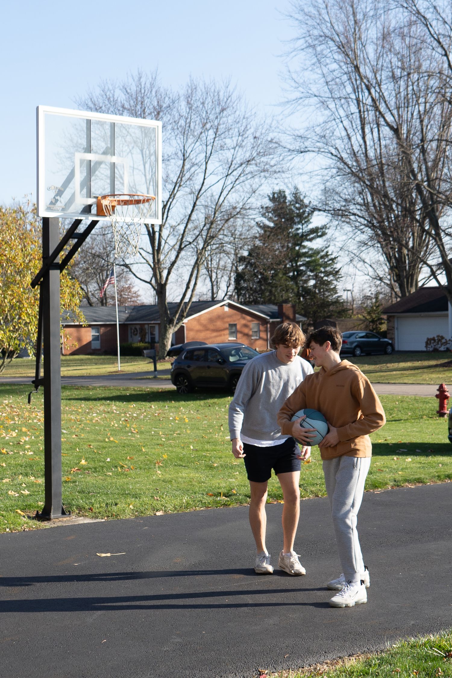 People play basketball on an outdoor court while falling leaves decorate the ground during autumn.