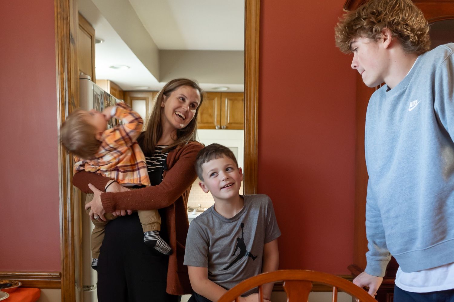 A candid group moment shows people laughing and interacting in a home hallway with red walls.