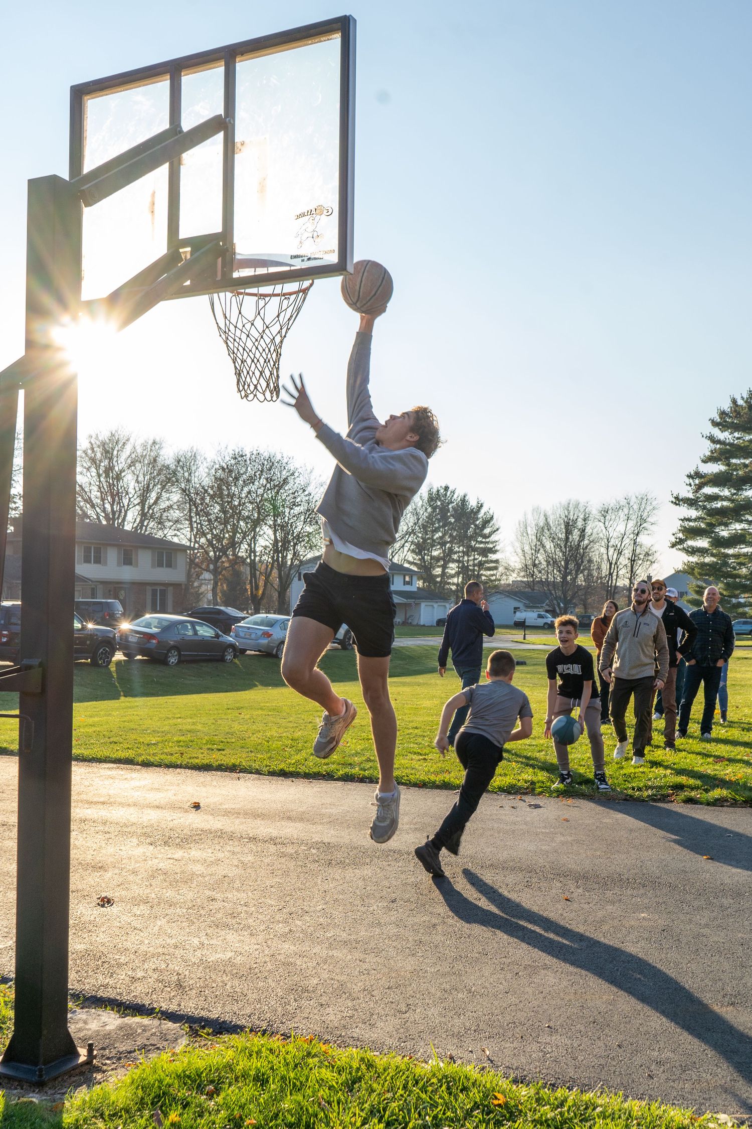 Two basketball players attempt to reach the ball during an outdoor pickup game at sunset on a paved court.