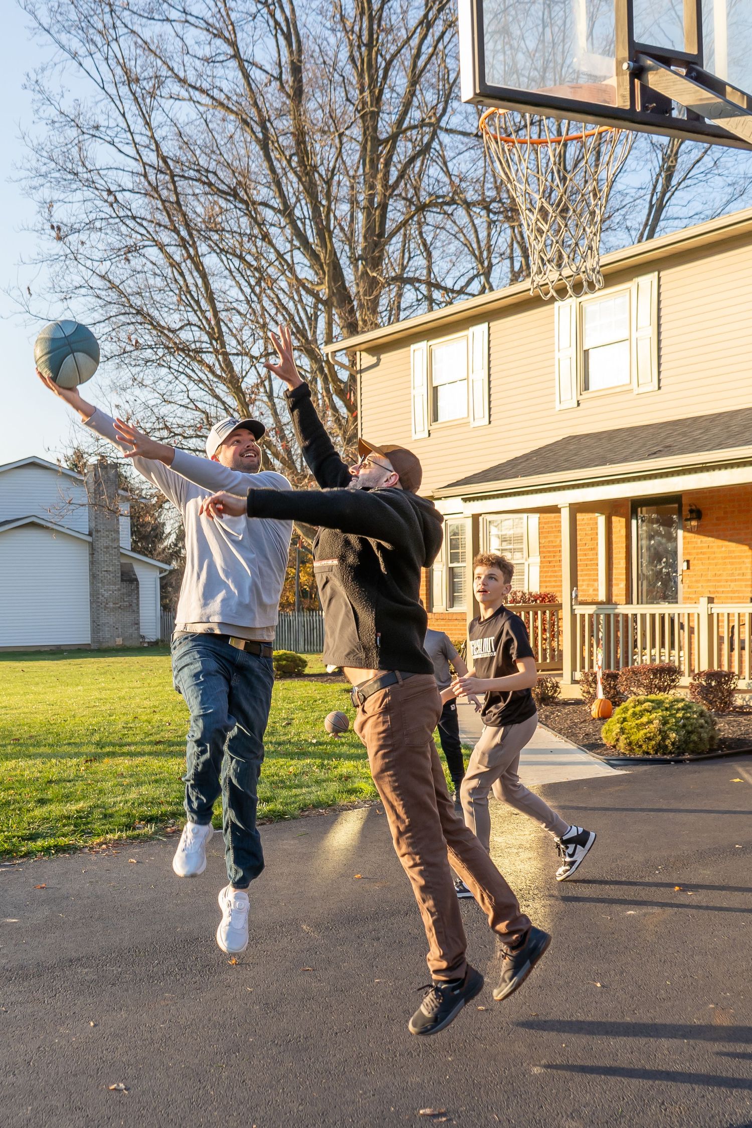 Group of youth playing basketball on a driveway court during a sunny afternoon at a residential home.