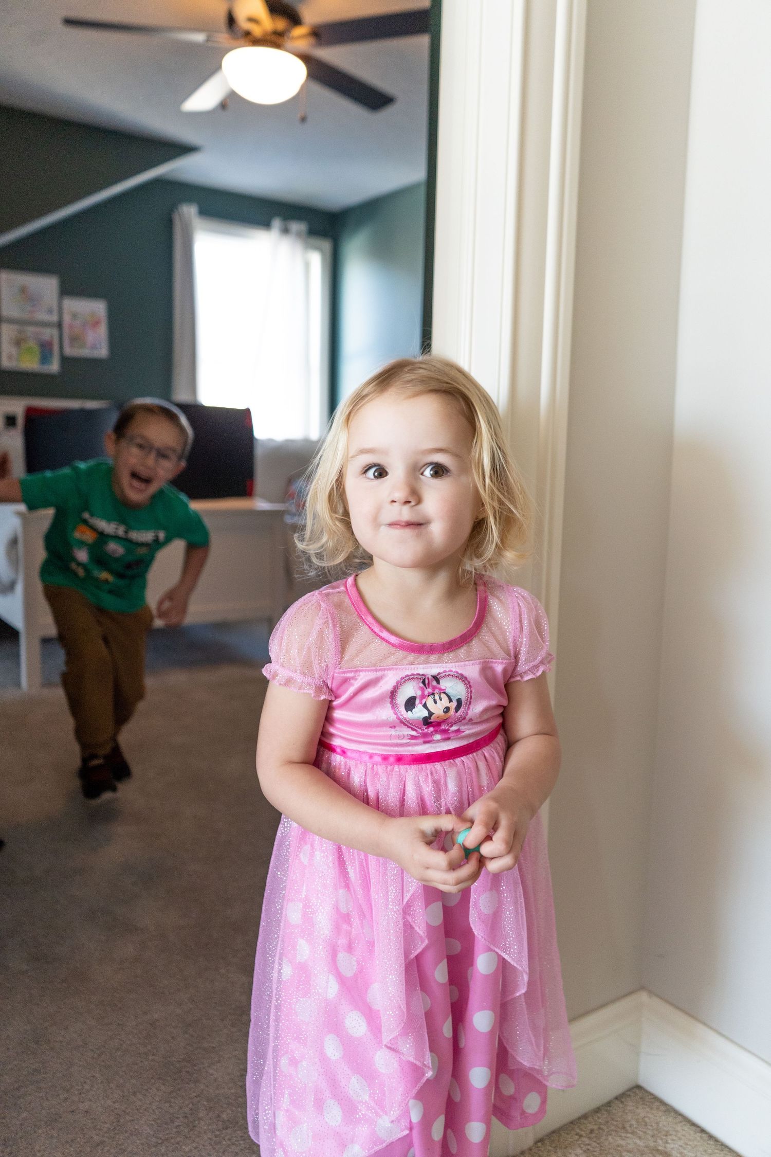 A child in a pink polka dot dress spins playfully in a hallway while another figure moves in the background.