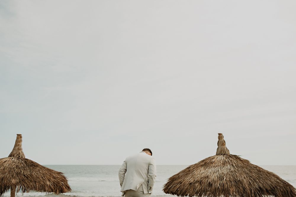 The groom waiting at the ceremony with the ocean and palm huts in the background
