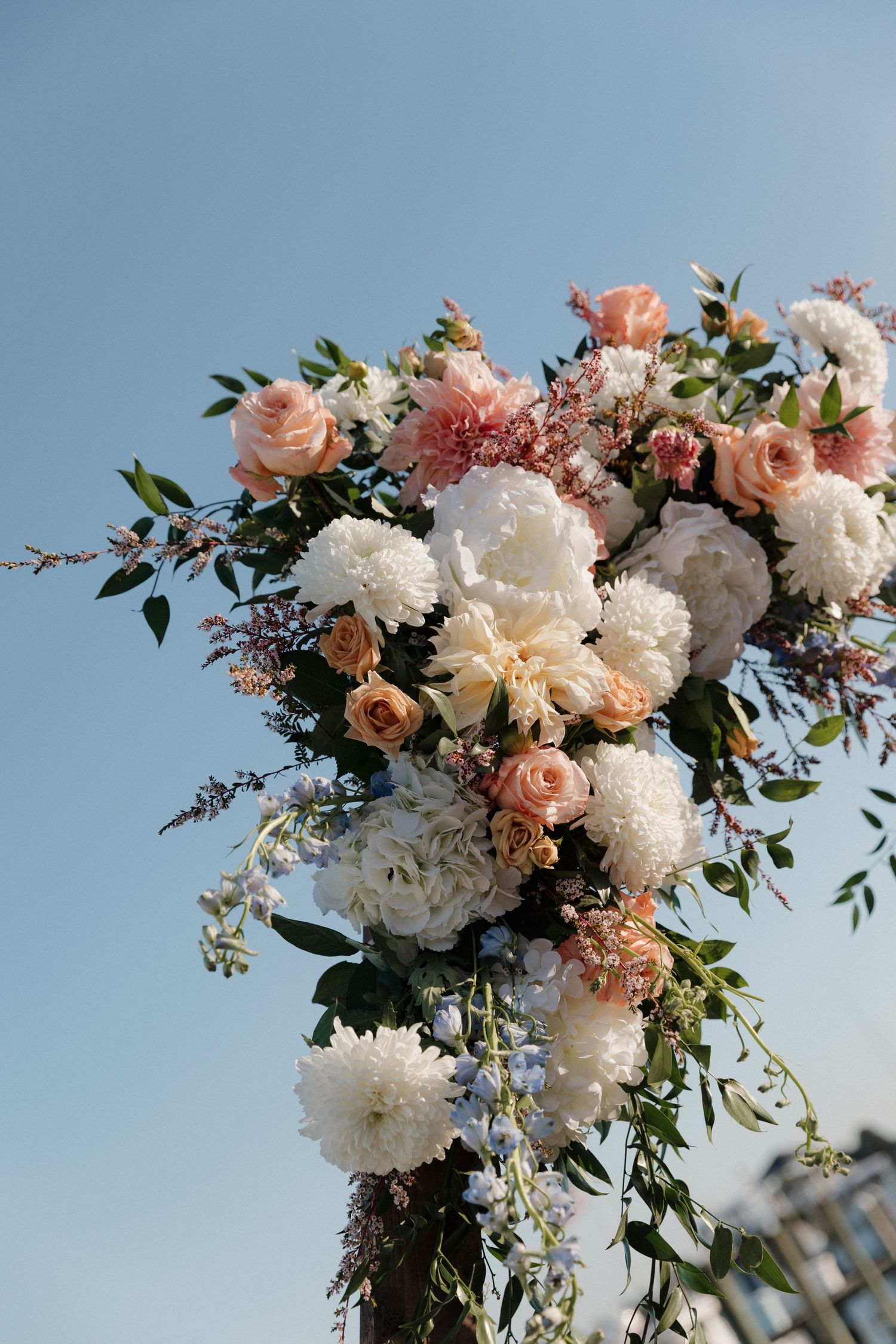 Beautiful floral wedding arch arrangement with white peonies, peach roses and greenery against a blue sky by the water dock in Connecticut.