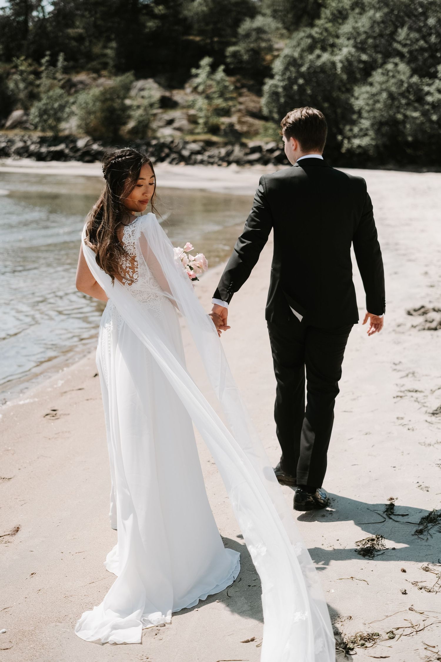 Newlyweds walking hand in hand on a beach with bride's dress flowing in the wind.