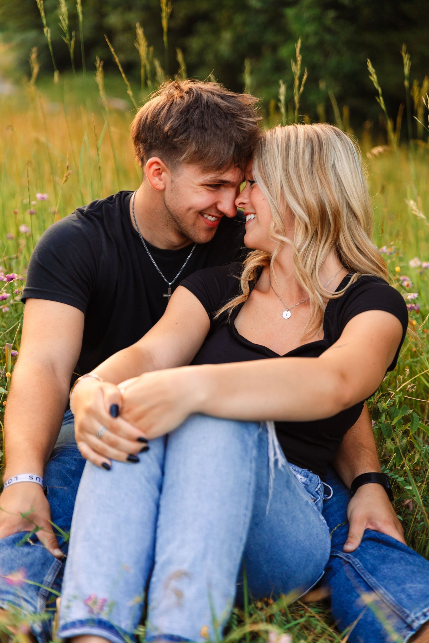 Intimate couple photos in casual wear sitting together in tall grass at sunset.