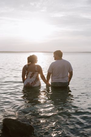 Couple sits together in shallow water watching a peaceful sunset over the lake.