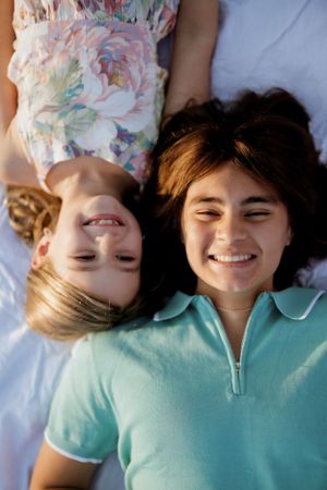 Friends laying down and smiling together on a blue blanket during a sunny day.