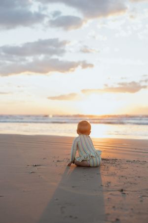 A silhouette of a child sitting on the beach during golden hour sunset.