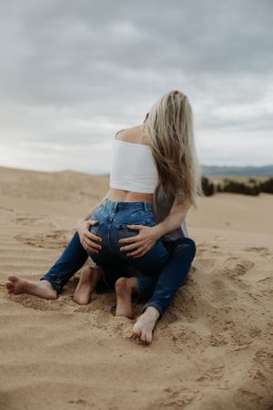 Intimate couple sitting on sand dunes in casual clothing.