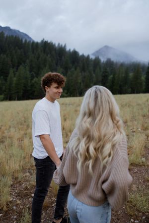 Romantic couple standing in mountain meadow with foggy forest landscape.