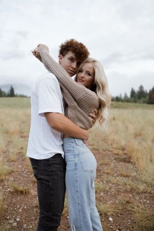 Young couple embracing in casual attire against mountain landscape backdrop.