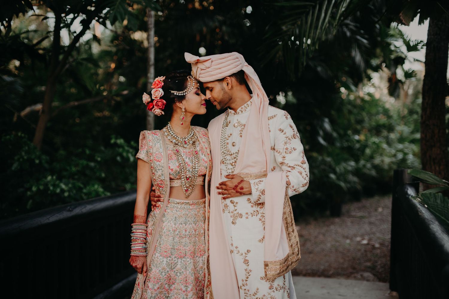 A romantic wedding couple in traditional South Asian attire embracing in a garden setting.