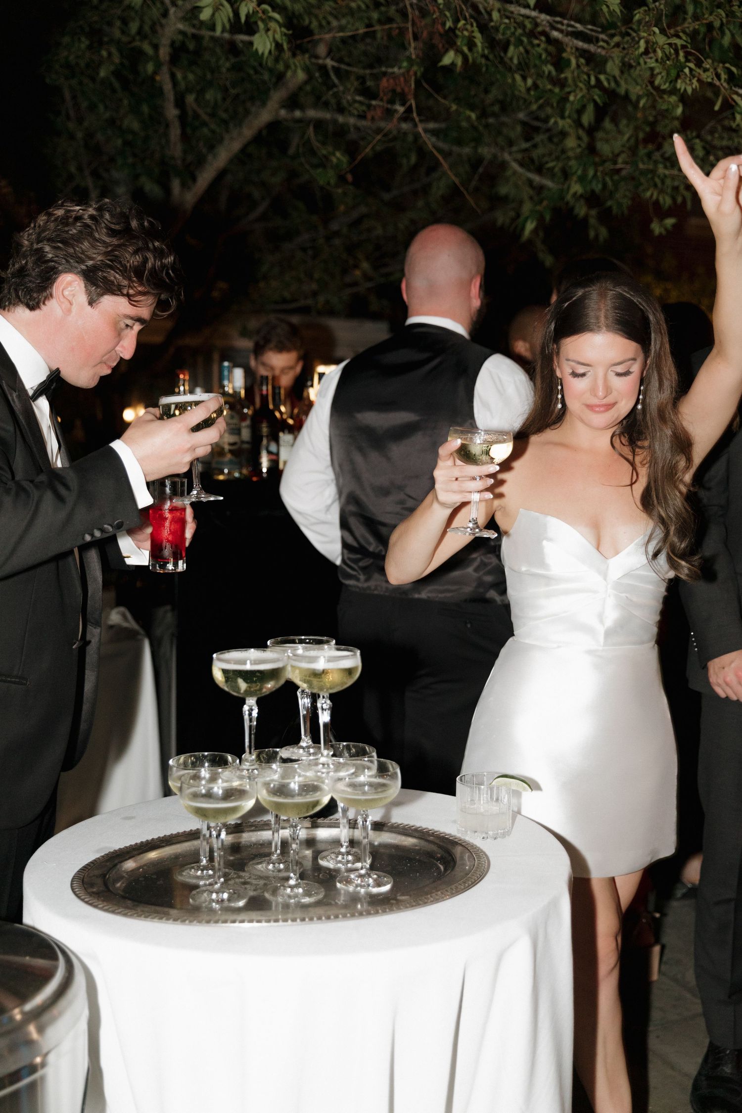 Flash photo of bride and groom around a champagne tower at an elegant evening wedding reception with coupe glasses on a silver tray in RI.