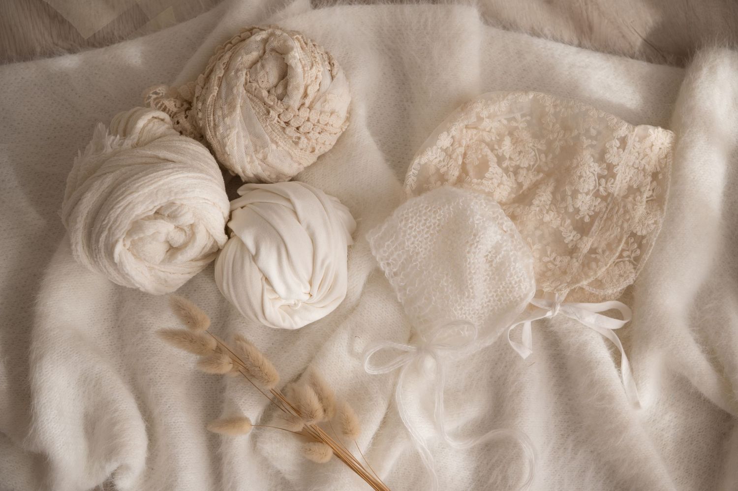 Delicate cream-colored fabric flowers and vintage lace arranged on soft white textile.