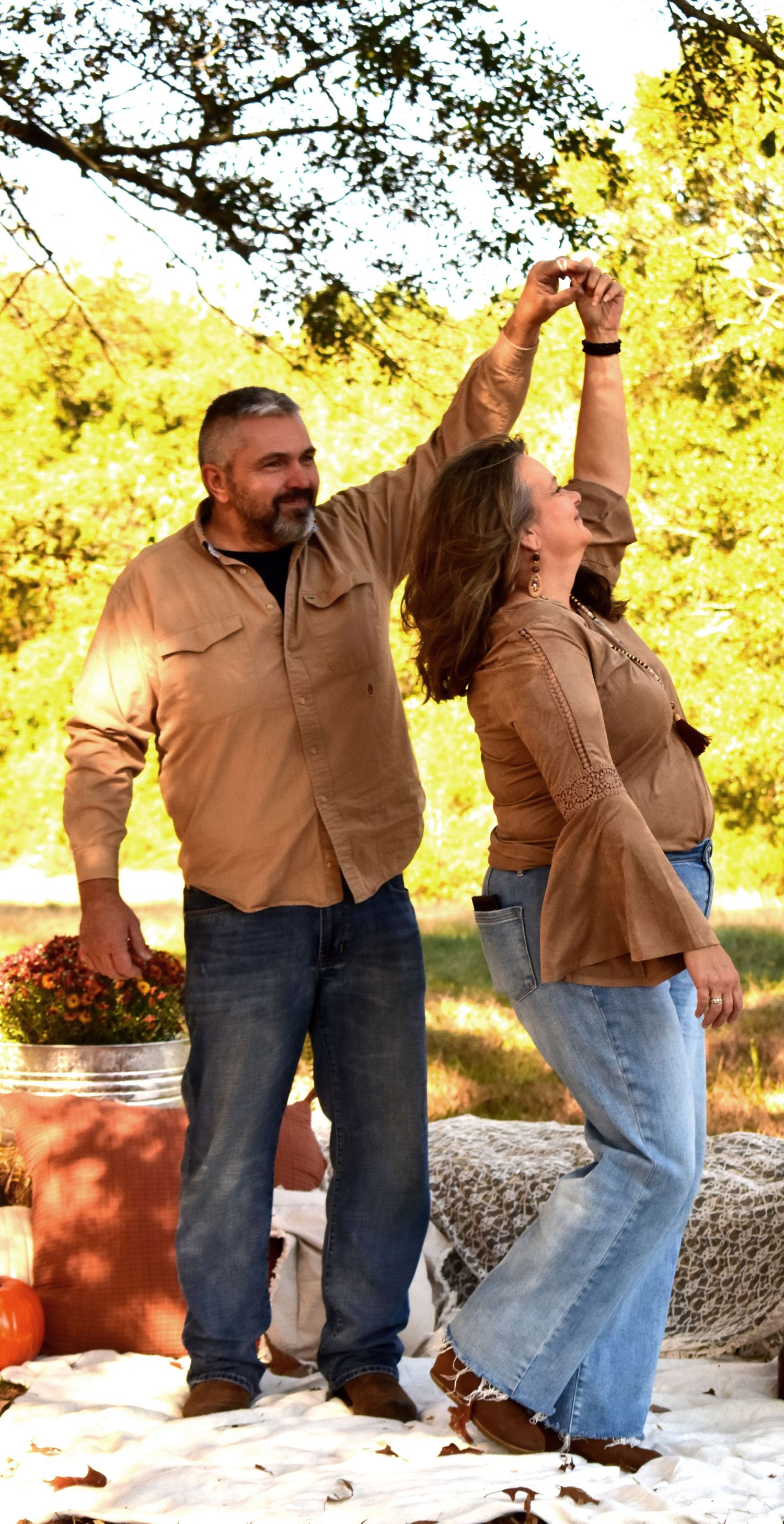 Couple dances outdoors on blanket surrounded by fall decor and golden sunlight.