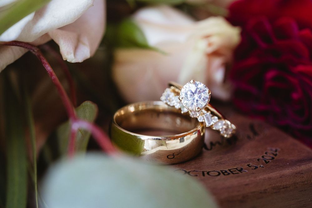 Close-up of elegant diamond engagement ring and wedding band nestled among flowers.