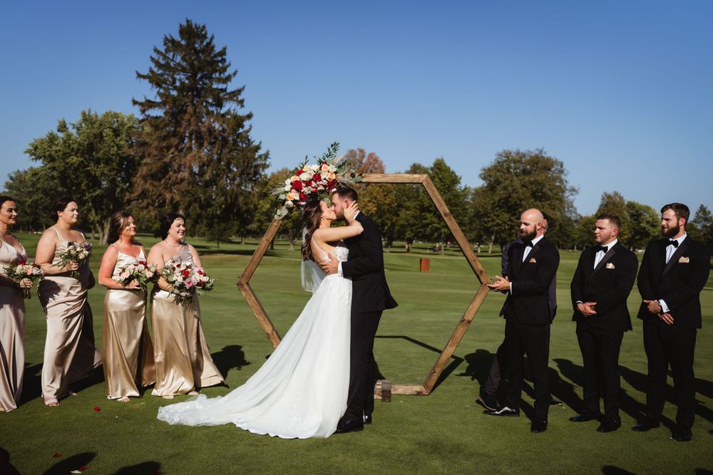 Wedding ceremony on a golf course with wedding party lined up under a hexagonal wooden arch.