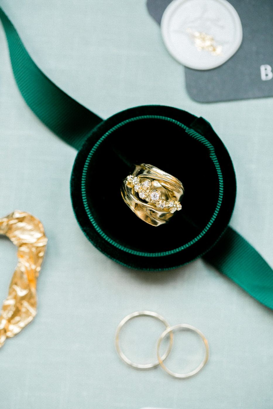 Ornate gold wedding ring nestled in dark green velvet box with matching ribbon.
