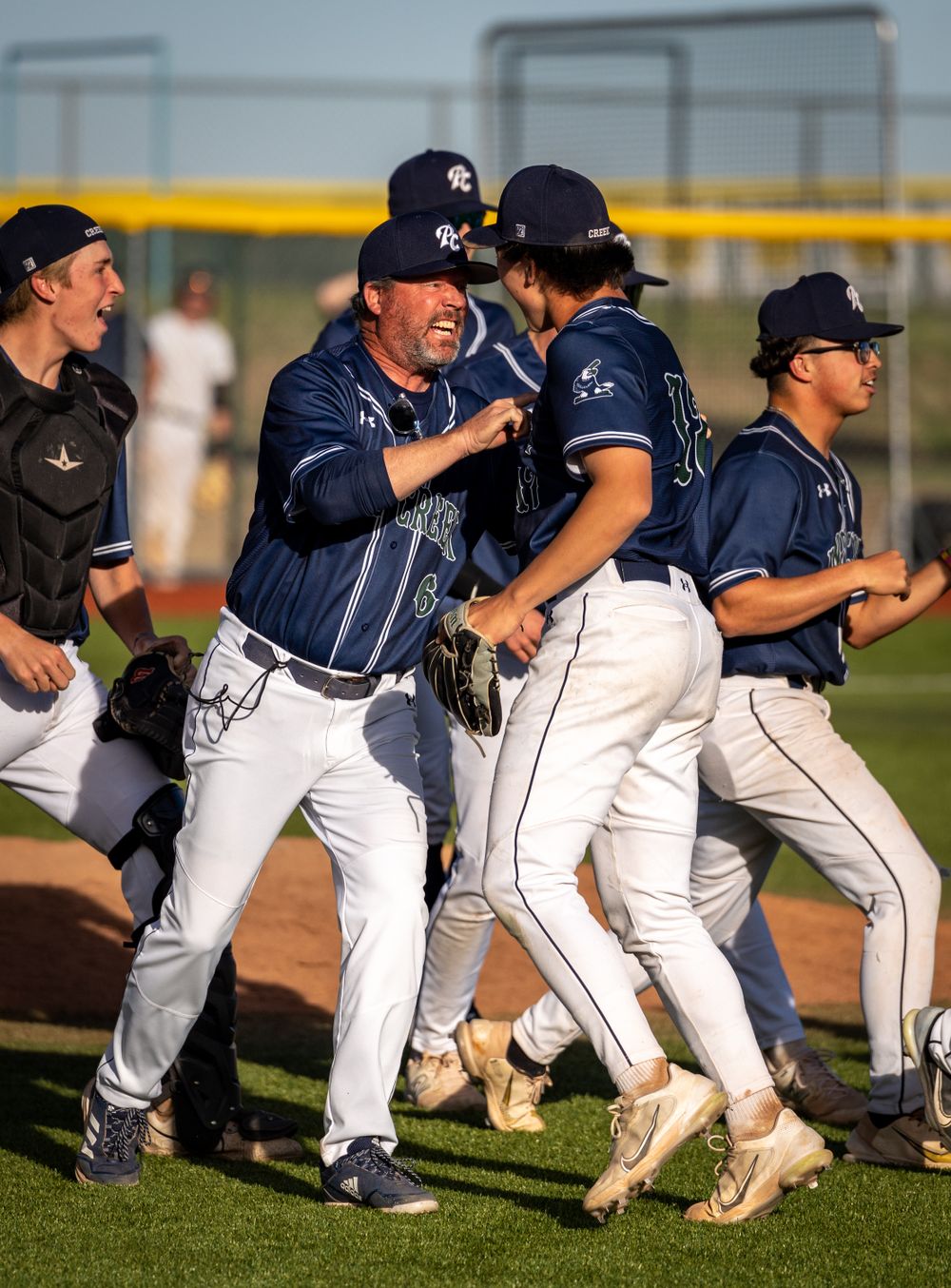 Baseball team celebrates victory on field with coaches and players hugging.