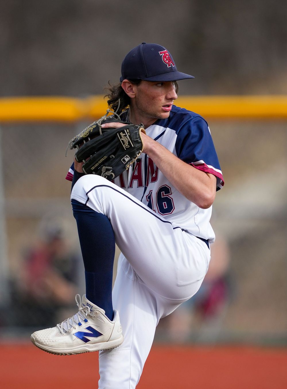 Baseball pitcher in wind-up position wearing navy and white uniform on mound.