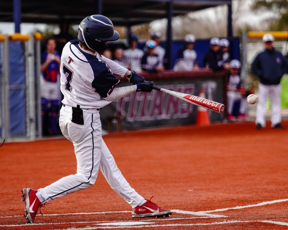 Baseball player in white uniform swings bat making contact with ball during game.