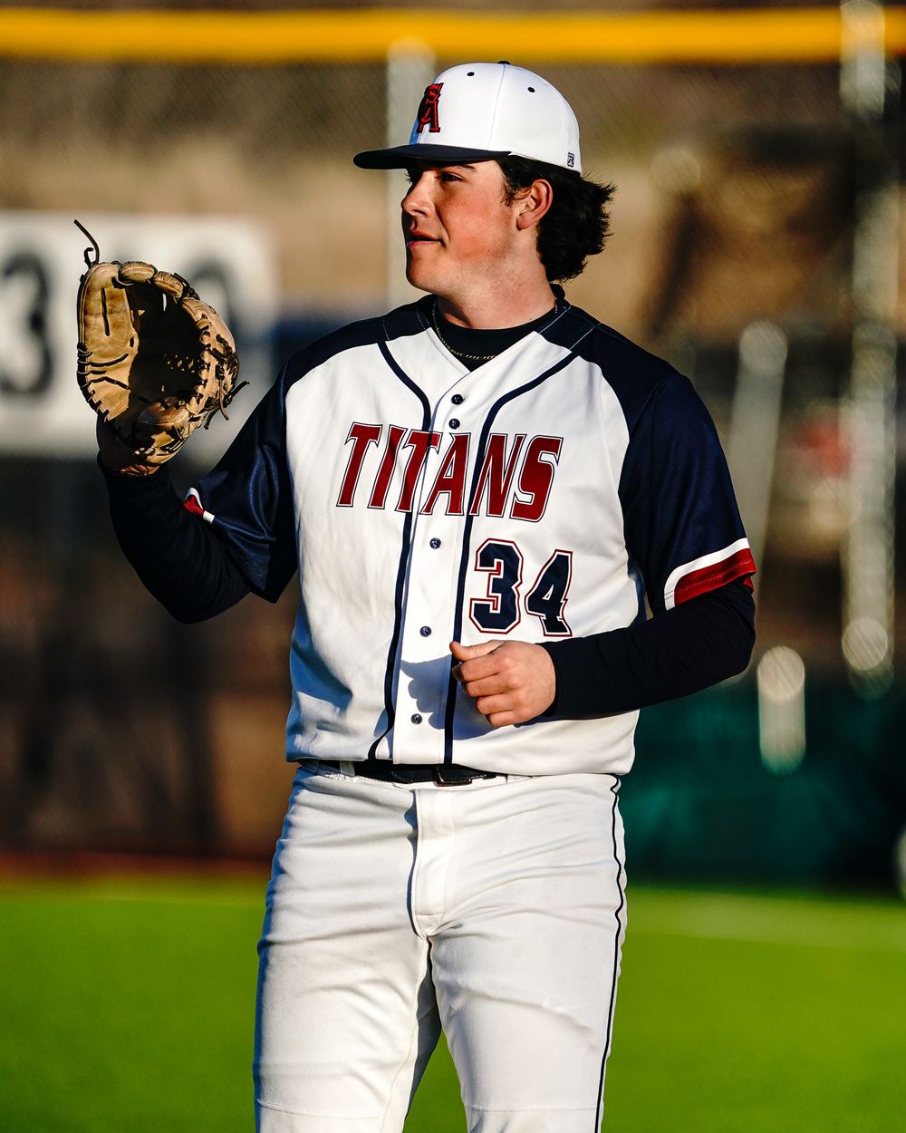 Baseball player in Titans uniform number 34 holds glove while standing on field.