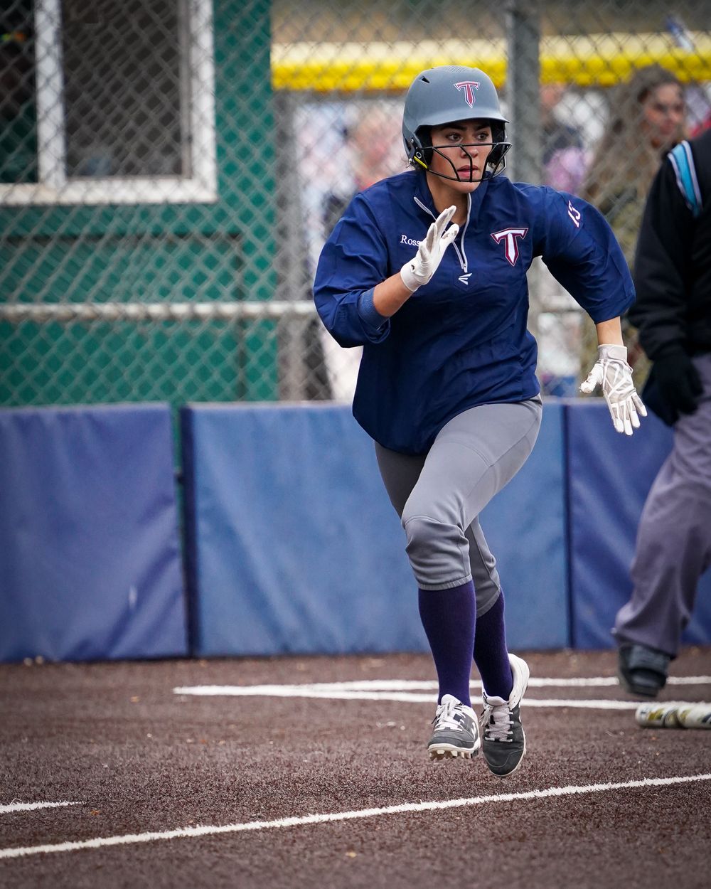 Softball player in navy uniform runs towards base during game.