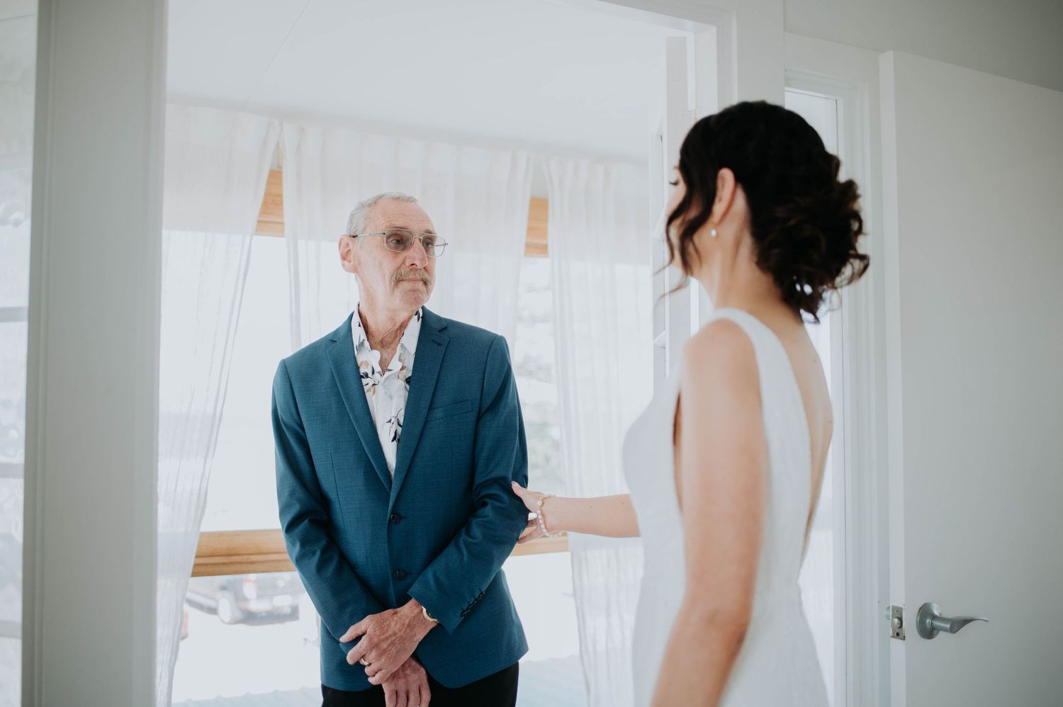 Emotional first look moment between bride and father in sunlit room.
