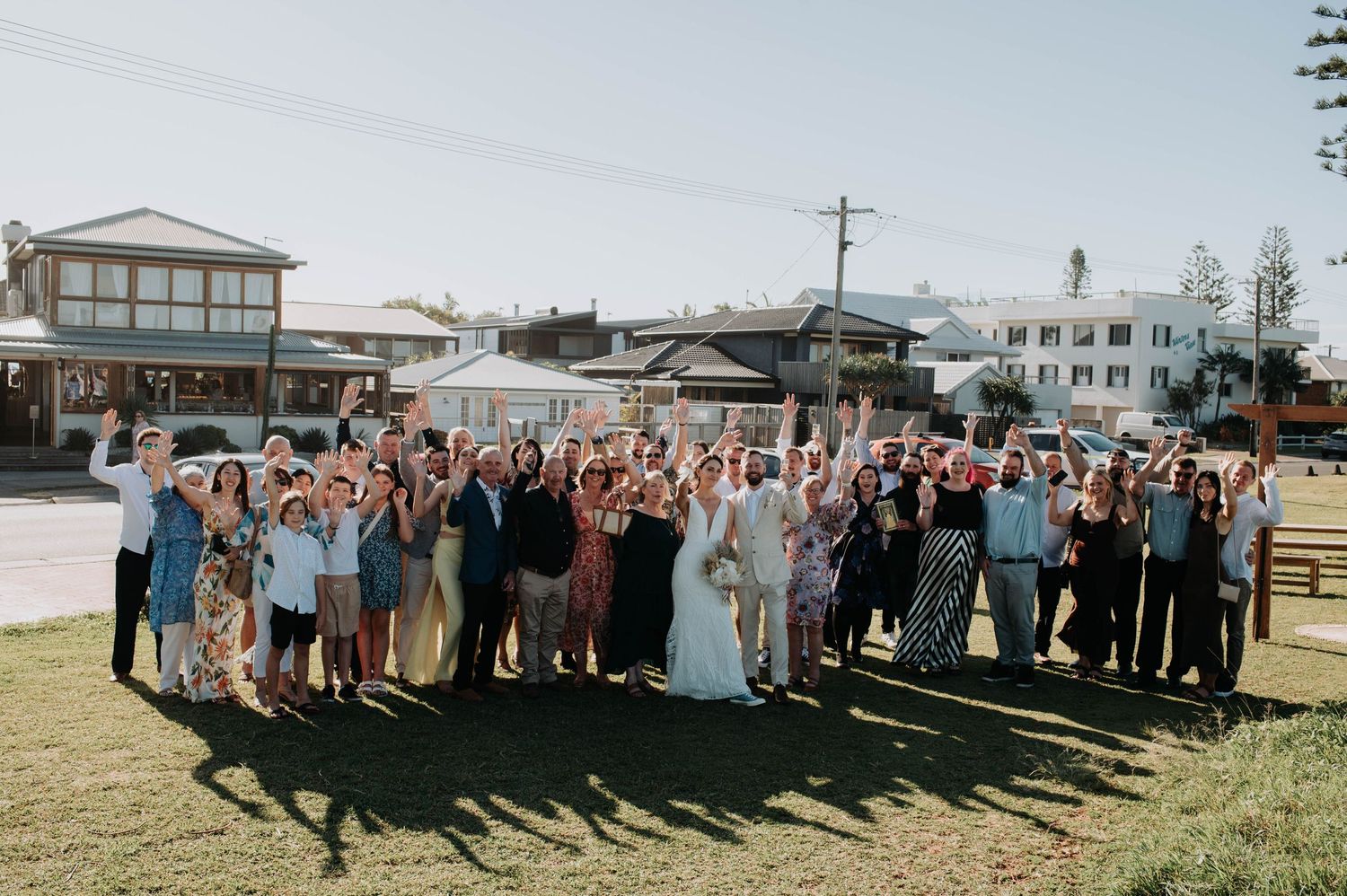 Large group of wedding guests posing together for a celebratory photo on a grassy lawn.