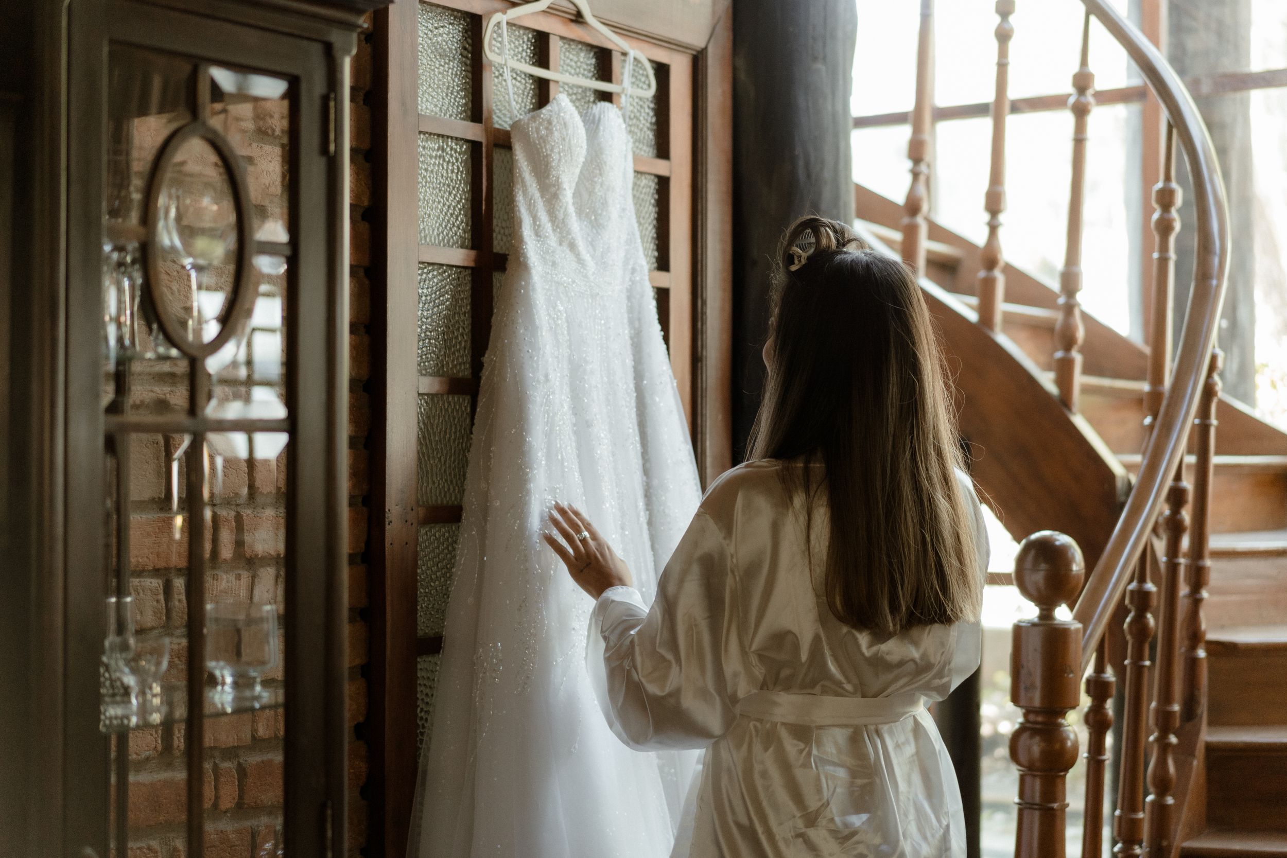 Back view of person admiring white wedding dress hanging in vintage interior setting.