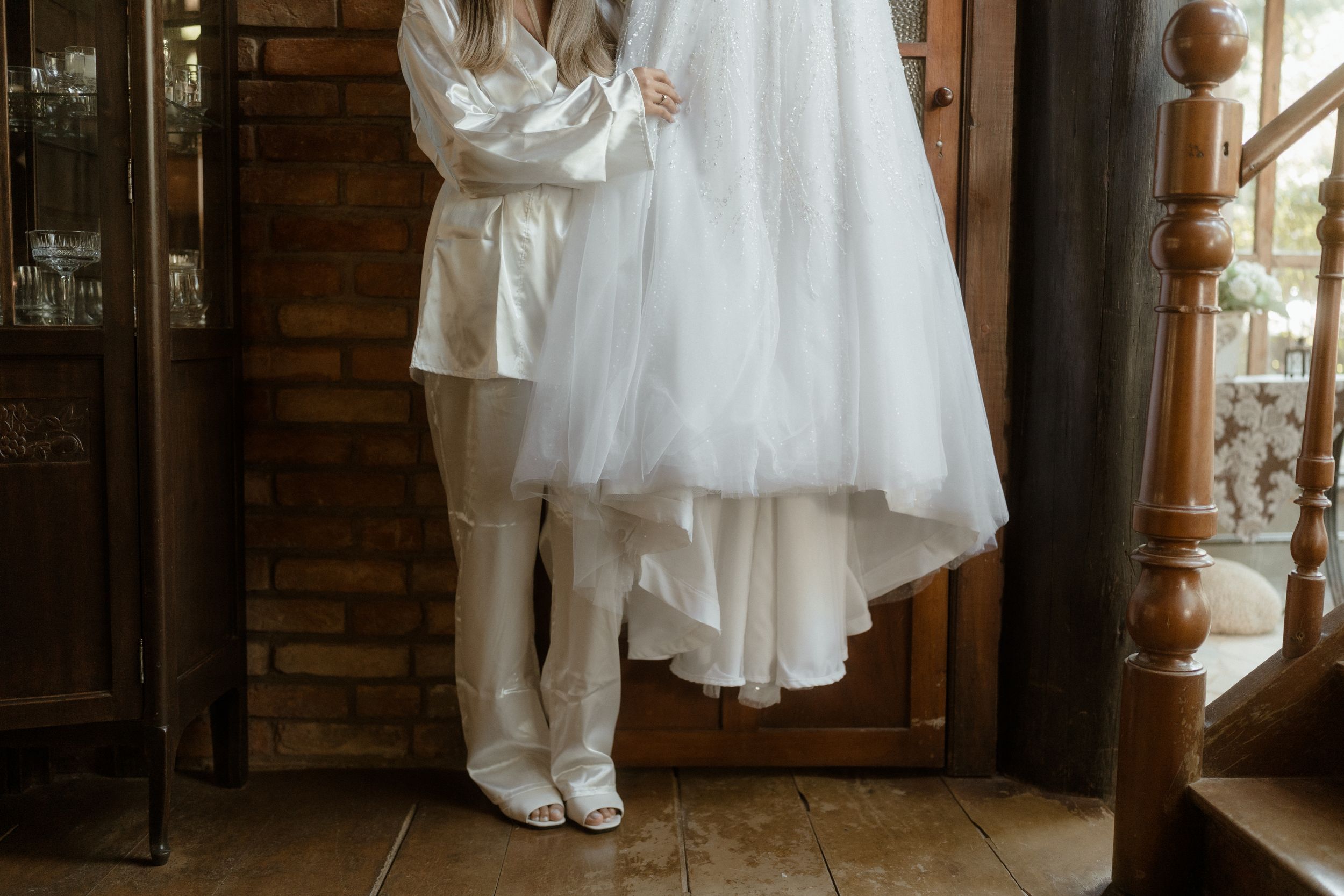 A sparkly white wedding dress hangs elegantly against a rustic brick wall in natural light.