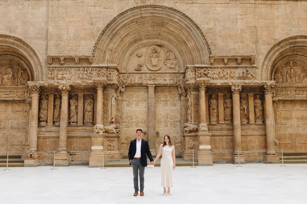 Couple standing before an ornate Romanesque stone church facade.