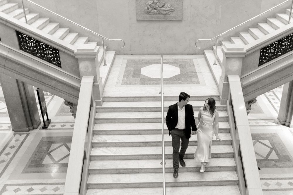 Black and white photo of couple descending elegant marble staircase.