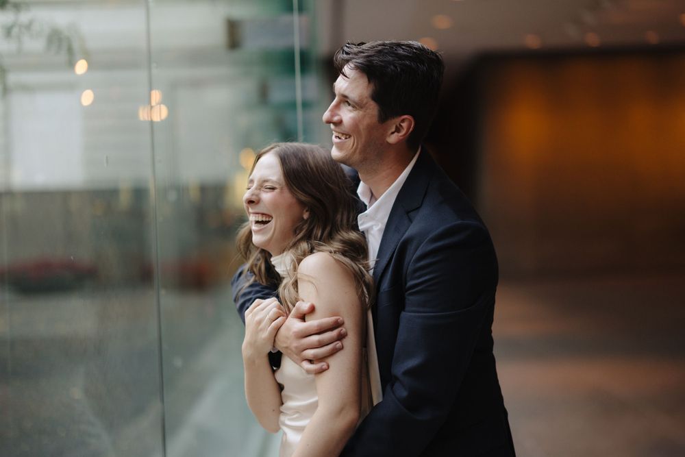 A joyful couple laughs together while embracing in an elegant indoor setting.