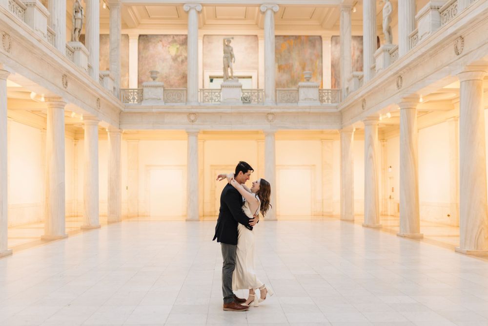 Couple dancing in a luxurious white marble hall with classical architecture.