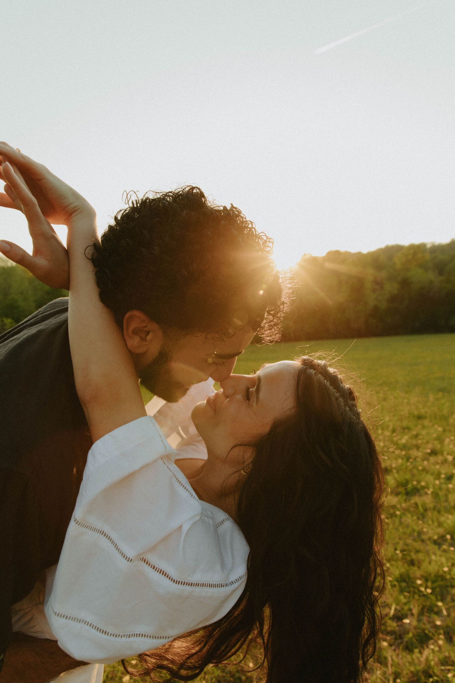 A couple shares a romantic moment in a sunlit field during golden hour.