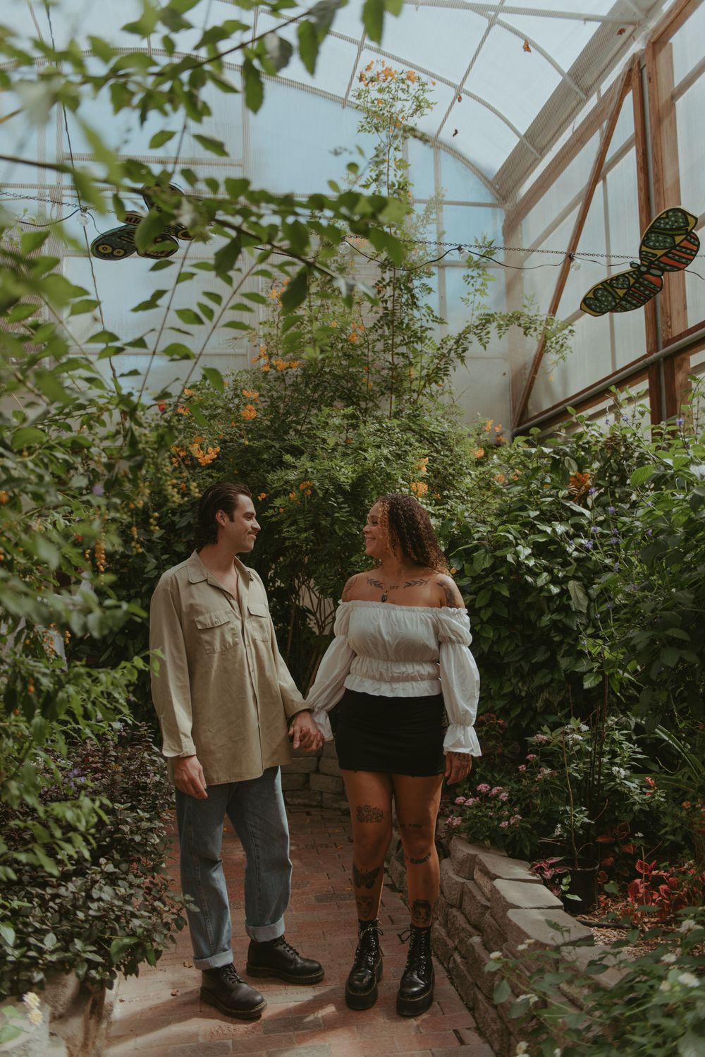 A couple are holding hands in a greenhouse.