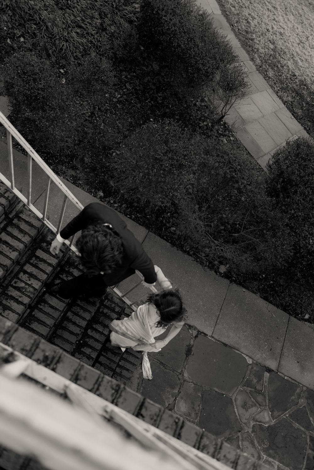 A black and white photo of a bride and groom walking up stairs.