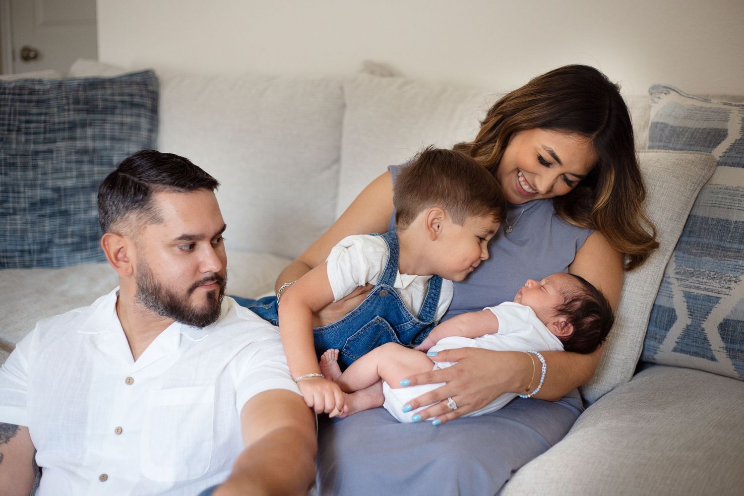 A family relaxes together on a gray couch while bonding with their newborn.
