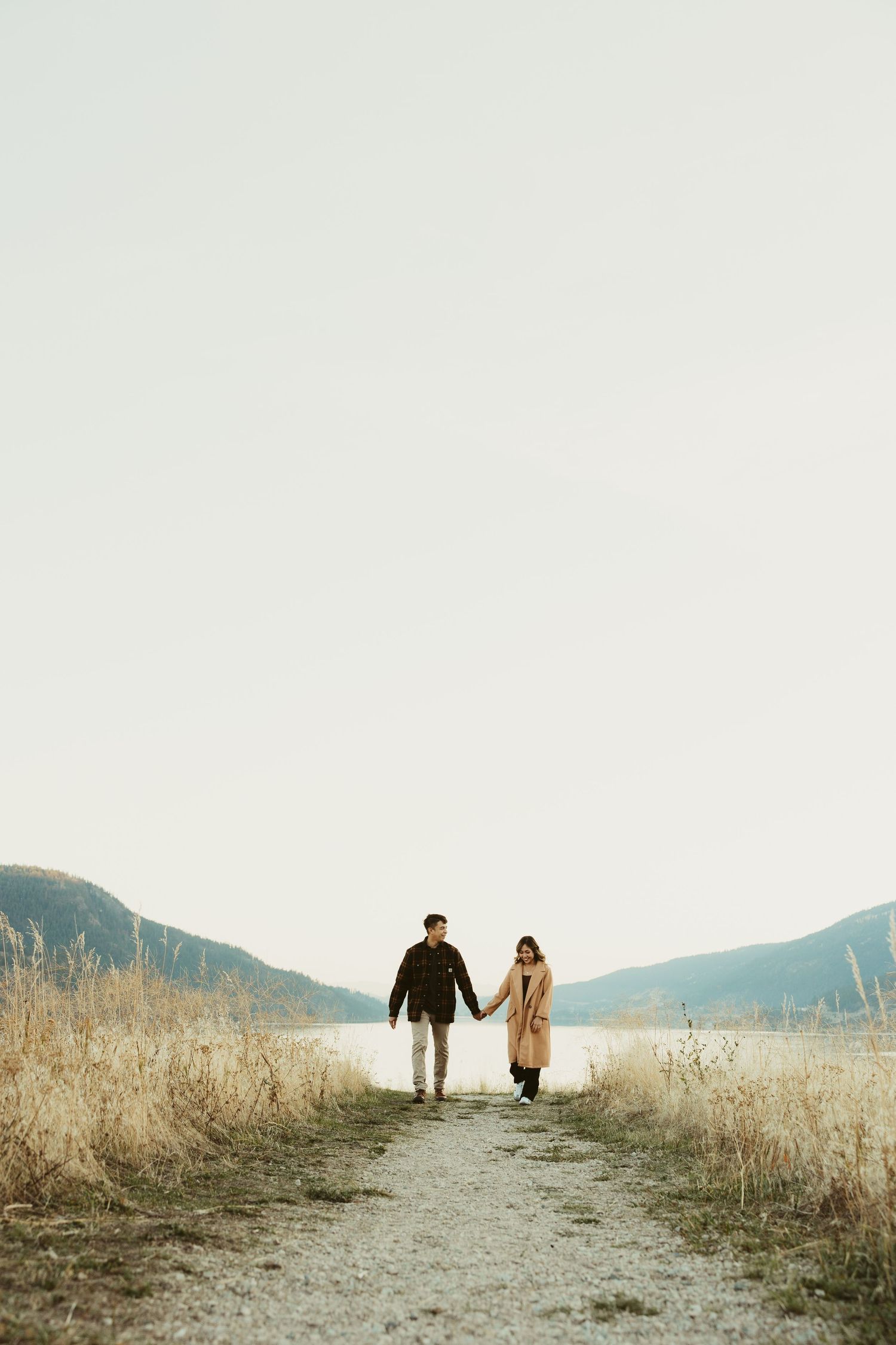 Couple walking down trail between mountains with lake view.