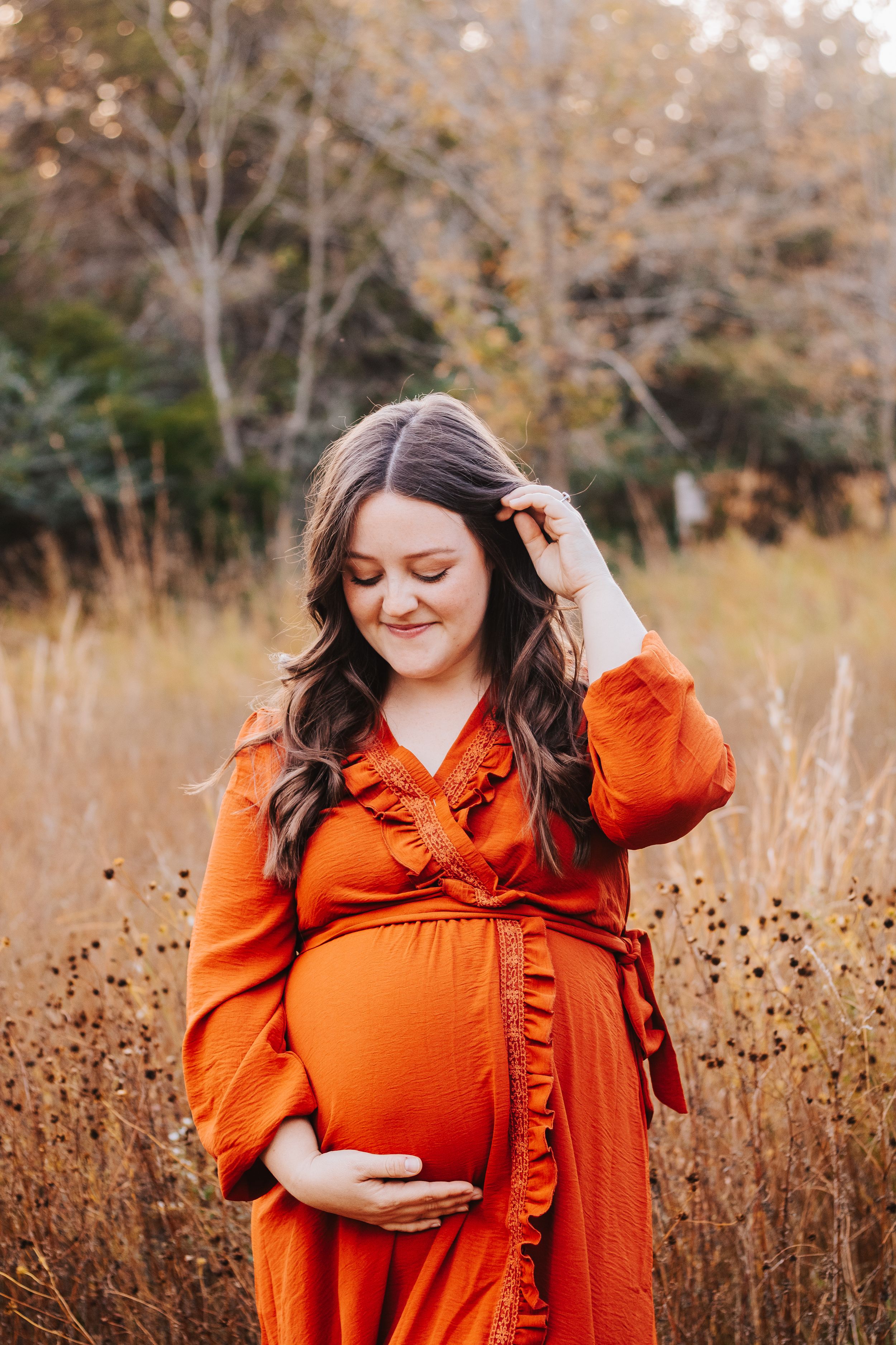 A person in a bright orange dress poses in a golden autumn field during sunset.