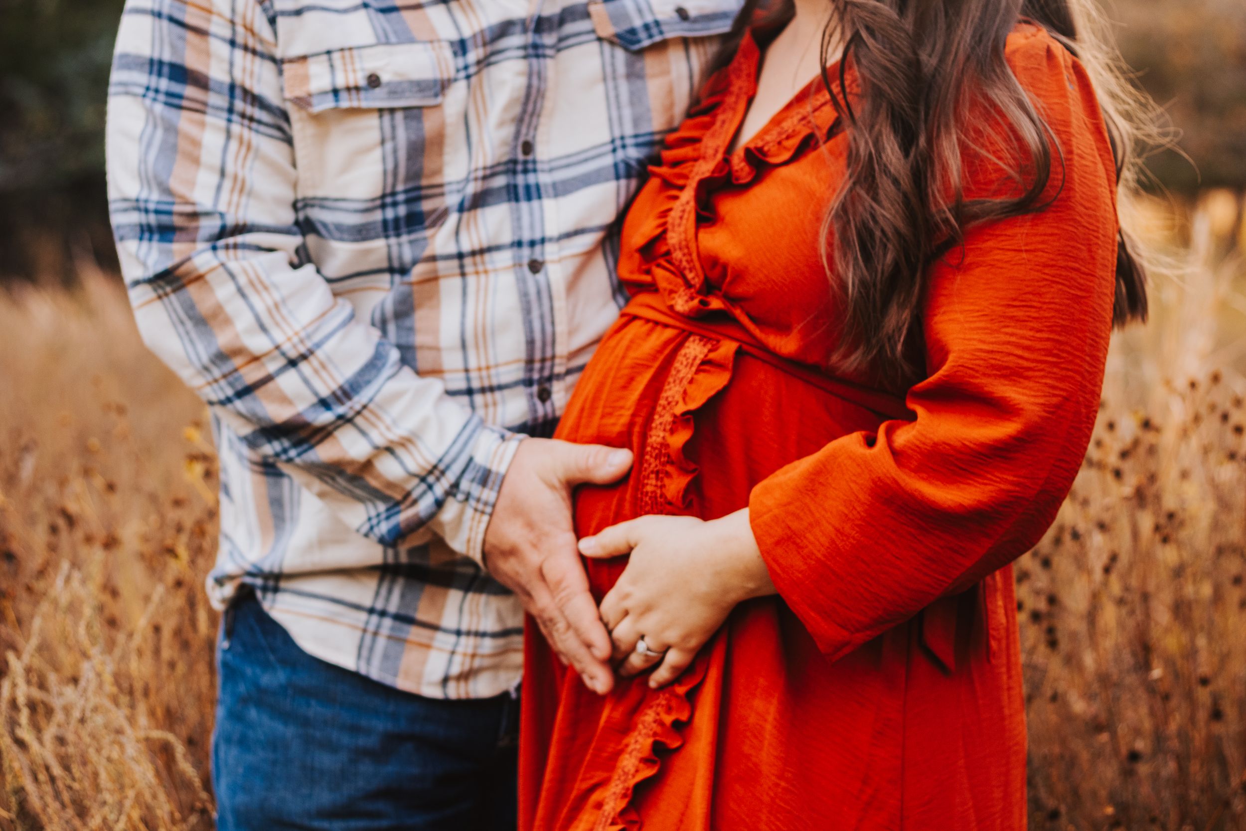 Couple embraces in autumn field with one wearing plaid and the other in orange.