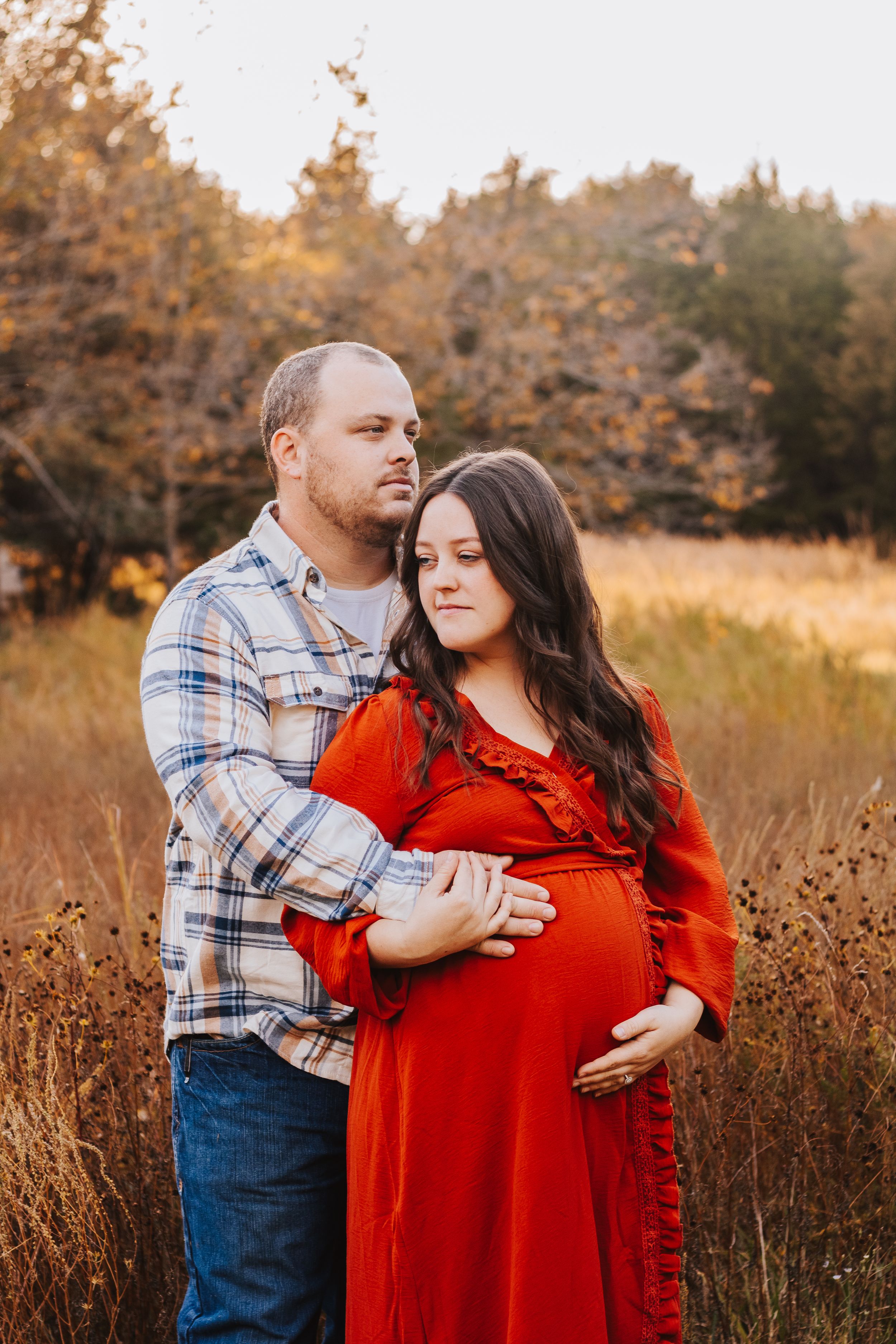 Couple embraces during maternity shoot in rustic fall setting.