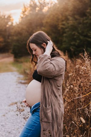 Artistic maternity portraits in brown sweater during golden hour.