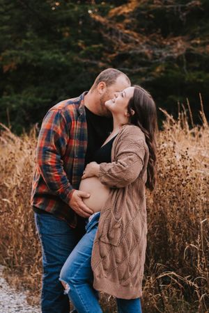 Intimate outdoor maternity photo session showing couple embracing in fall field with golden grass.