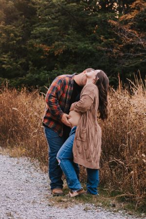 Romantic maternity photoshoot with couple standing together against autumn field backdrop.